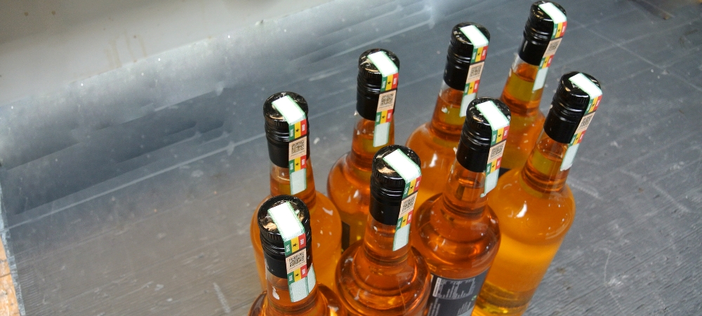 Automatisk forsegling af flasker med tax labels. Labels påsættes toppen og ned langs siden af flasken